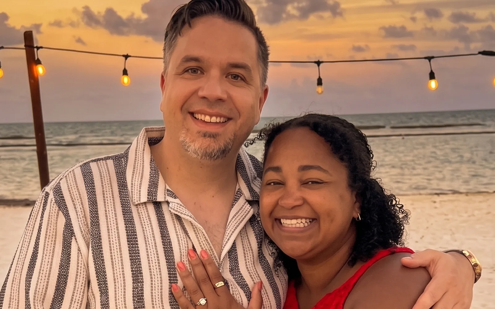 Jennifer and Joe together on the beach at sunset, string lights overhead